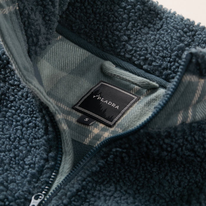 Close-up of Men's Cypress Sherpa Fleece in Atlantic Blue by Pladra, with plaid lining and label near the zipper.