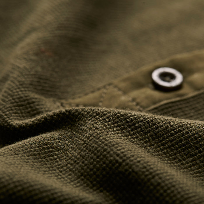 Close-up of Pladra Men's Elko Henley in Forest Green, showing textured cotton waffle fabric, black button, and seam.