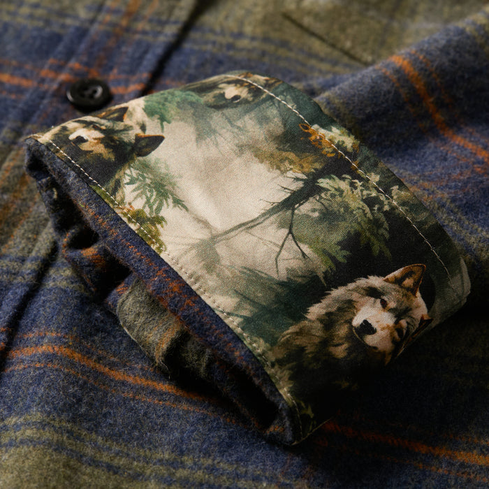 A close-up of the Men's Every Day Flannel Shirt in Everett Green Heather shows its olive, blue, and brown plaid pattern with the cuff folded back to reveal an inner lining adorned with wolves and trees.