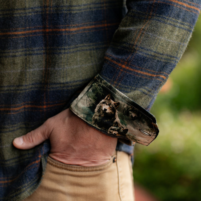 A person in tan pants wears the Men's Every Day Flannel Shirt - Everett Green Heather, with the cuff turned up to show a wolf-illustrated lining and one hand in their pocket.