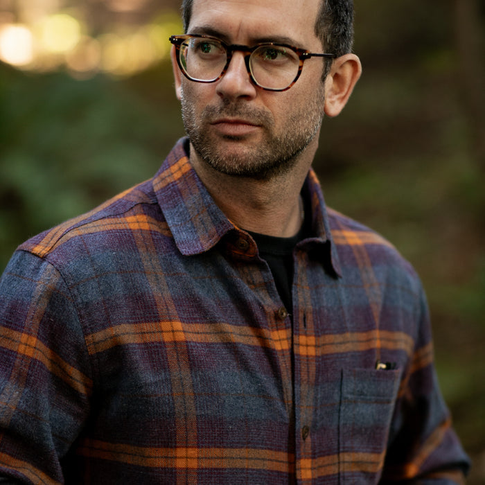 Man with glasses wears Pladra Men's Every Day Flannel Shirt in Portsmouth Blue Heather, looking thoughtfully to the side.