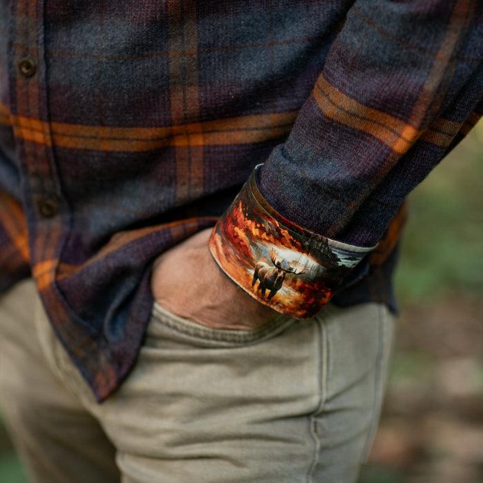 A person in khakis wears the Pladra Men's Every Day Flannel Shirt in Portsmouth Blue Heather with a moose-print cuff.