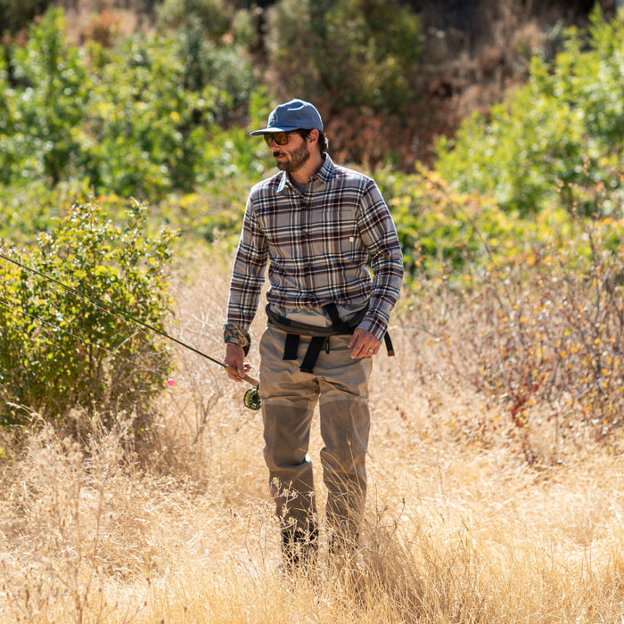 Man in a Pladra Men's Every Day Flannel Shirt - Richmond Grey fly fishing in a field with tall grass and green bushes.