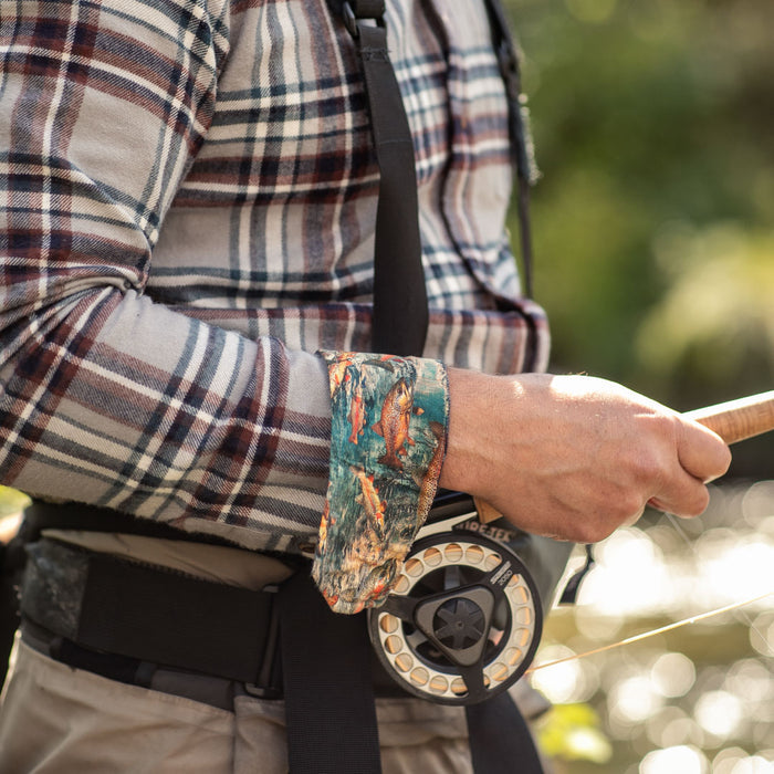 Wearing a Pladra Men's Every Day Flannel Shirt in Richmond Grey, a man holds a fishing rod by the sunlit river.