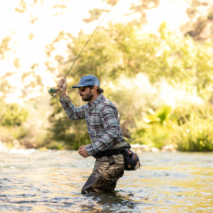 Man fly fishing in a river, wearing Pladra Men's Every Day Flannel Shirt- Richmond Grey, cap, and waders.