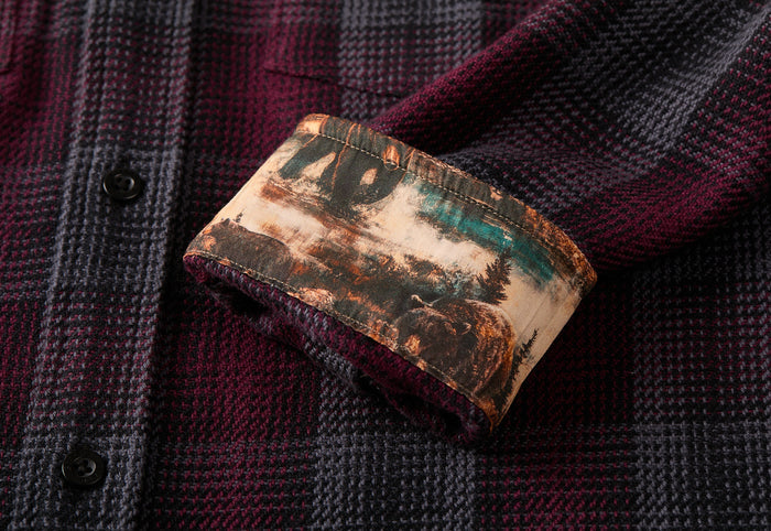A close-up of the Men's Fireside Flannel - Hickory Red sleeve shows the cuff turned up, revealing an inner lining with a scenic outdoor pattern featuring trees and a river.