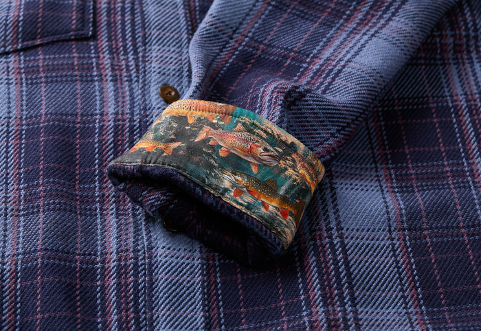 The Men's Fireside Flannel - Riffle Blue by Pladra features blue plaid and trout-patterned cuffs in soft organic cotton.