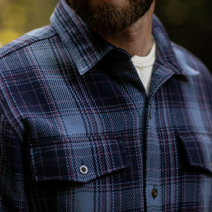 A man in the Pladra Men's Fireside Flannel - Riffle Blue over a white t-shirt, shown from shoulders to upper chest.