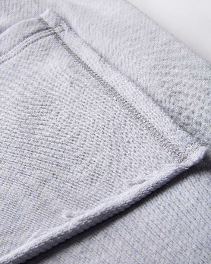 Close-up of light gray tracksuit bottoms showing a folded corner with raw, frayed hems and a stitched seam.