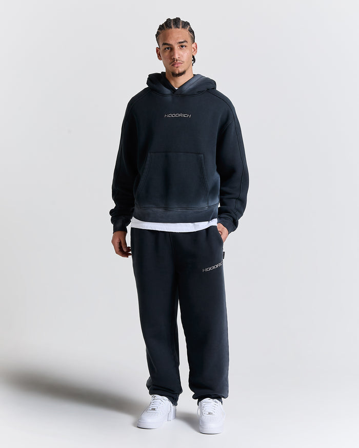 Person wearing a black hoodie and pants with 'Hoodrich' branding on a light gray background