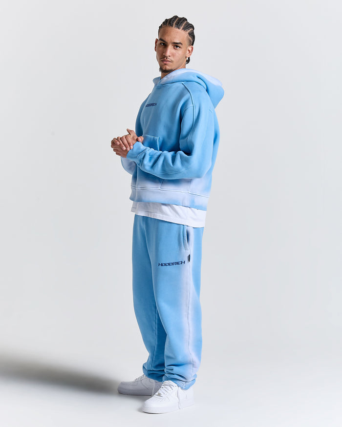 Person wearing a light blue tracksuit with a white shirt on a plain background