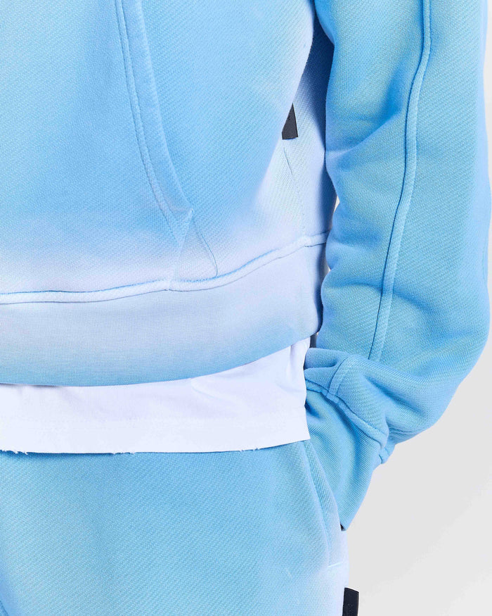 Close-up of the Hoodrich logo embroidered on the chest of an oversized blue hoodie.