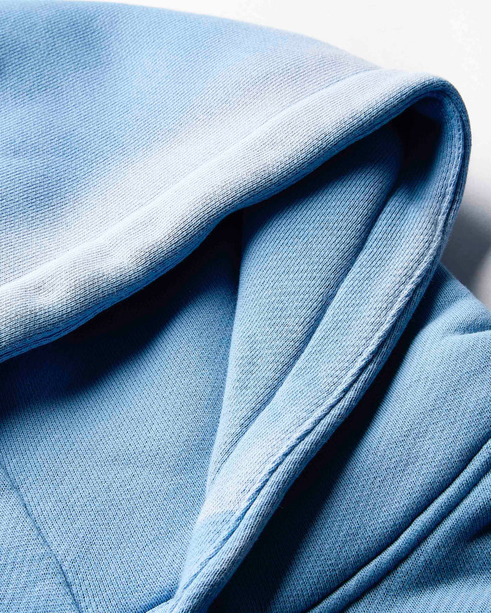 Extreme close-up of the embroidered Hoodrich logo on the blue fabric of the hoodie.