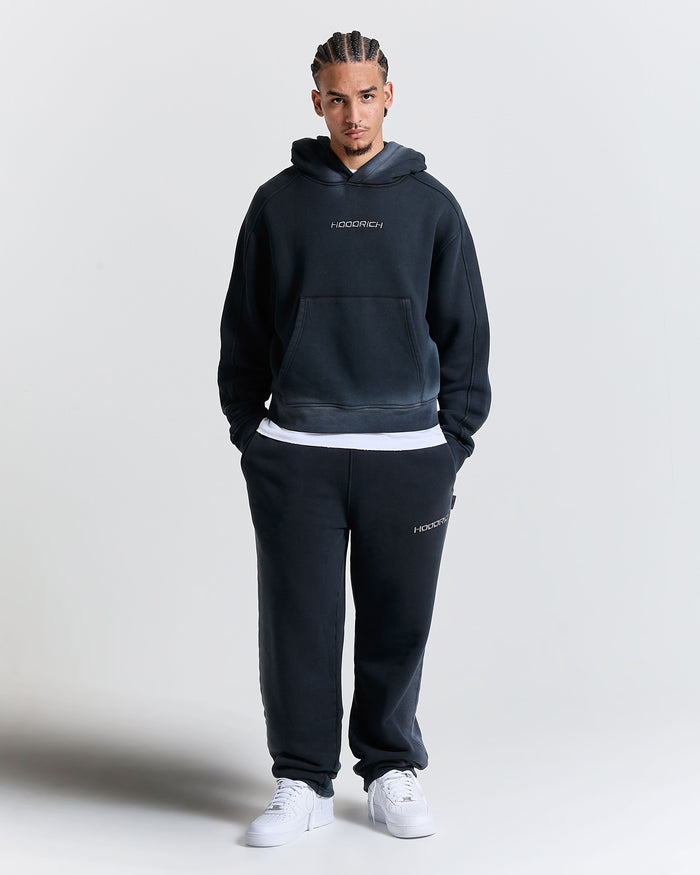 Man wearing a black hoodie and pants with 'Hoodrich' branding on a light gray background