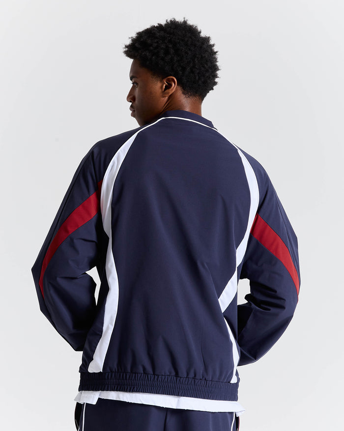 Person wearing a navy tracksuit with red and white accents on a light gray background