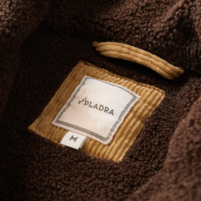 A close-up of a Pladra Men's Ironwood Sherpa Jacket in Acorn Tan with size M on the inner corduroy pocket.