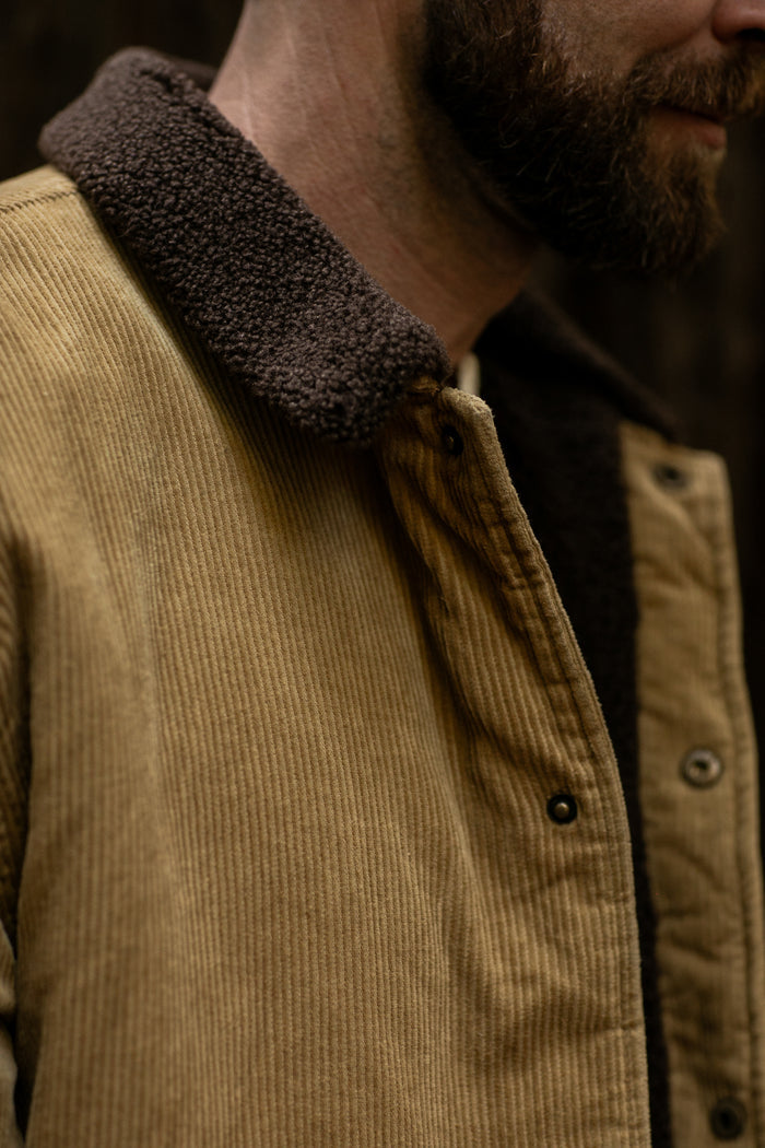 Close-up of Pladra Men's Ironwood Sherpa Jacket in Acorn Tan with dark brown collar, lower face only visible.