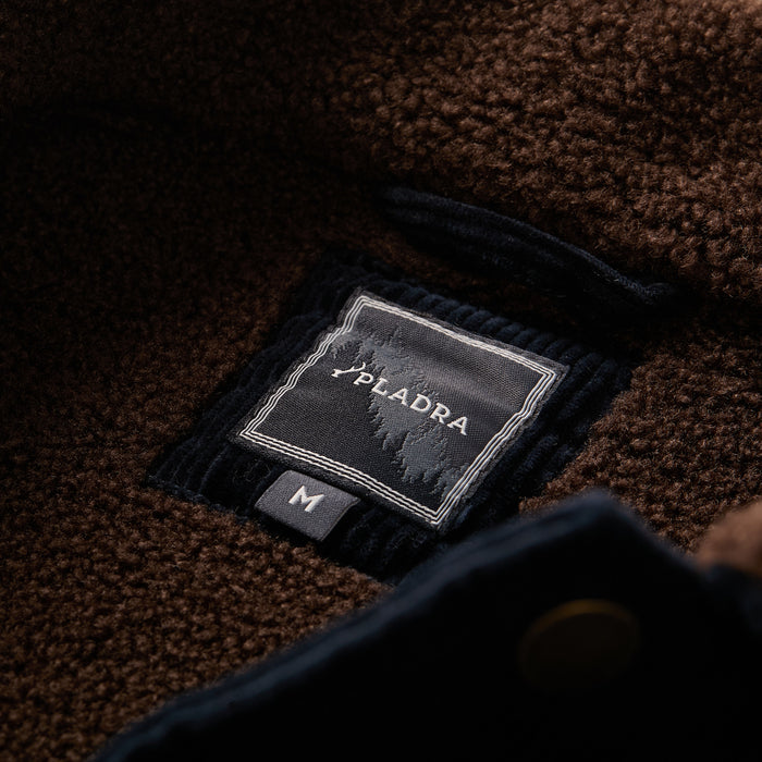 Close-up of the Men's Ironwood Sherpa Jacket in Midnight Blue, featuring textured fleece with a PLADRA fabric label displaying a mountain design and a size M tag below.