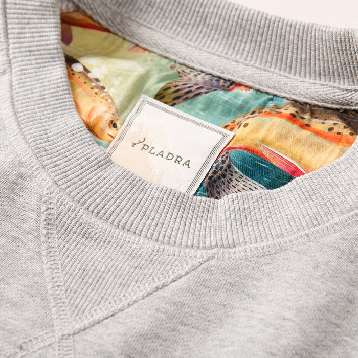 Close-up of the Men's Klamath Crew in Fog Grey, featuring a PLADRA label on the collar. The French terry interior showcases a vibrant fish pattern with greens, oranges, and detailed scales.