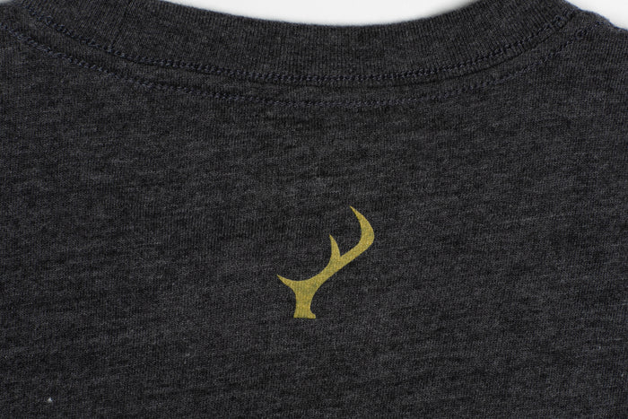 Pladra Men's Quail Tee in Charcoal Grey Heather features a small yellow antler graphic below the collar.