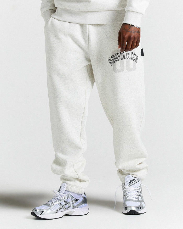 Person wearing light gray sweatpants with a brand logo and white sneakers on a white background