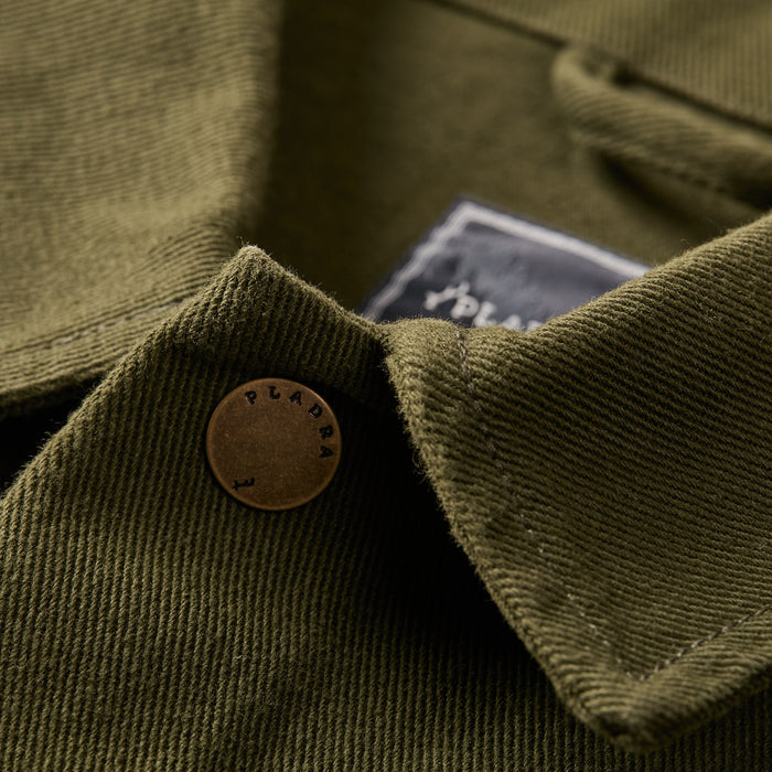 Close-up of Pladra Men's Sequoia Chore Coat in Hunter Green, showing brass button and black label on collar.