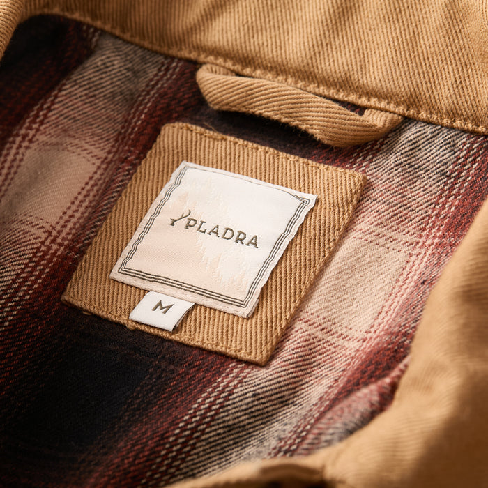 Close-up of Men's Sequoia Jacket–Tobacco Brown inner collar, showing plaid lining and Pladra label with size M tag.