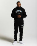 Displays a model wearing the Black 'Hoodrich' branded men's Shadow Full Tracksuit