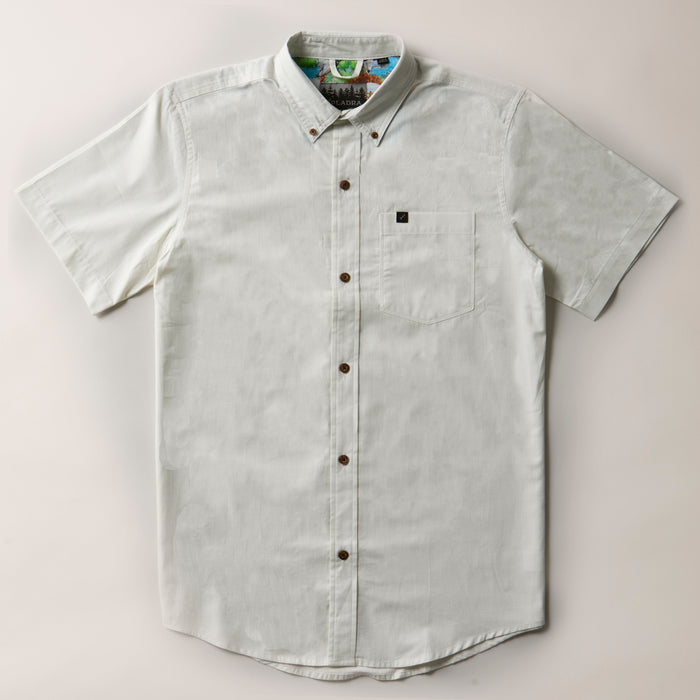 The Men's Short Sleeve Tailwinds Shirt in Sand White Chambray is a lightweight cotton button-up with a collar, front chest pocket, and brown buttons, shown laid flat on a light background.