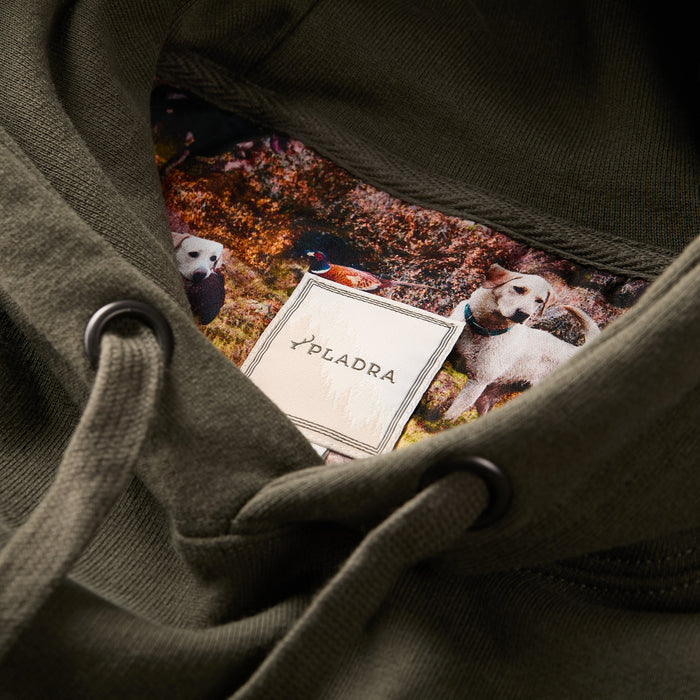Close-up of the Men's Sierra Hoodie- Pine Green neckline, crafted from premium cotton, featuring a Pladra brand tag and colorful lining with an outdoor scene of two dogs and a duck.