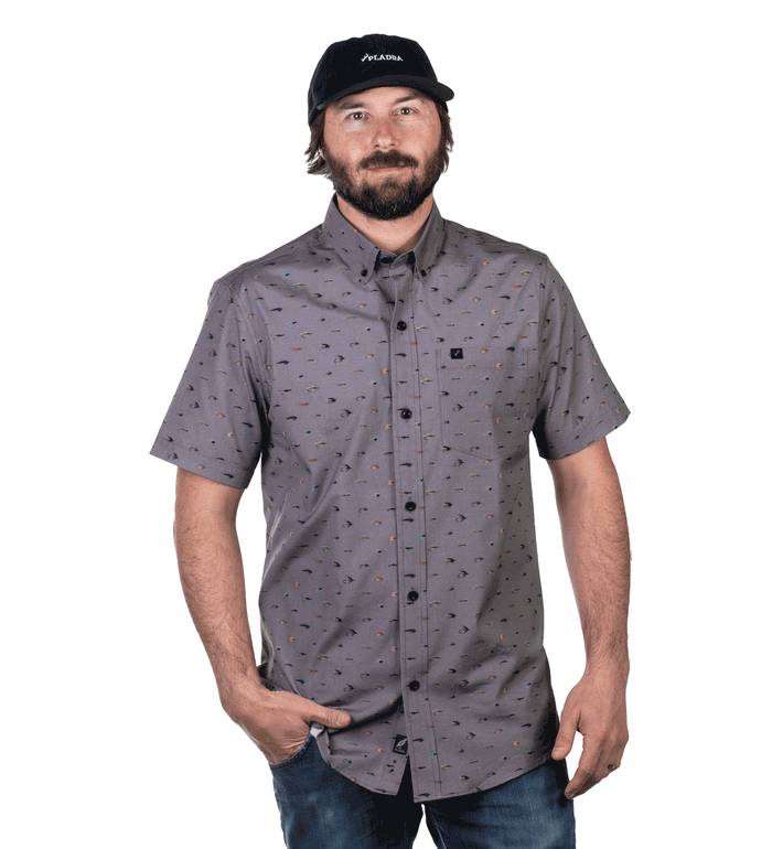 Man in Pladra’s Men's S/S Printed Outdoor Aloha Shirt - Steelhead Flies, blue jeans, and black cap, hand in pocket.