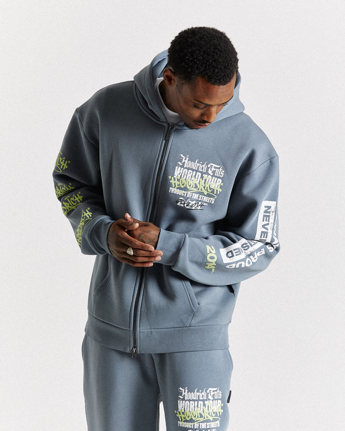 A man wearing a matching gray zip-up hoodie and sweatpants set with white and green graphic text details, photographed against a light gray studio background.
