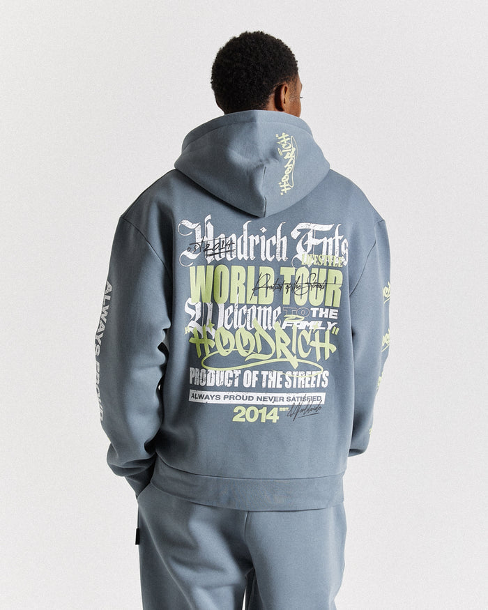 A man viewed from behind wearing a slate blue-gray Woodrich Endz World Tour hoodie with large graphic text on the back, paired with matching pants, against a light gray studio background.