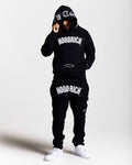 Person wearing a black 'Hoodrich' hoodie and pants on a white background