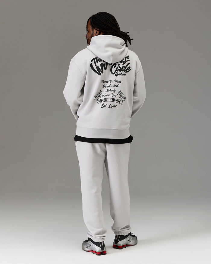 A model shown from the back wearing a white hoodie with a large black graphic print on the back, paired with white sweatpants and black and red sneakers, against a neutral gray studio background.
