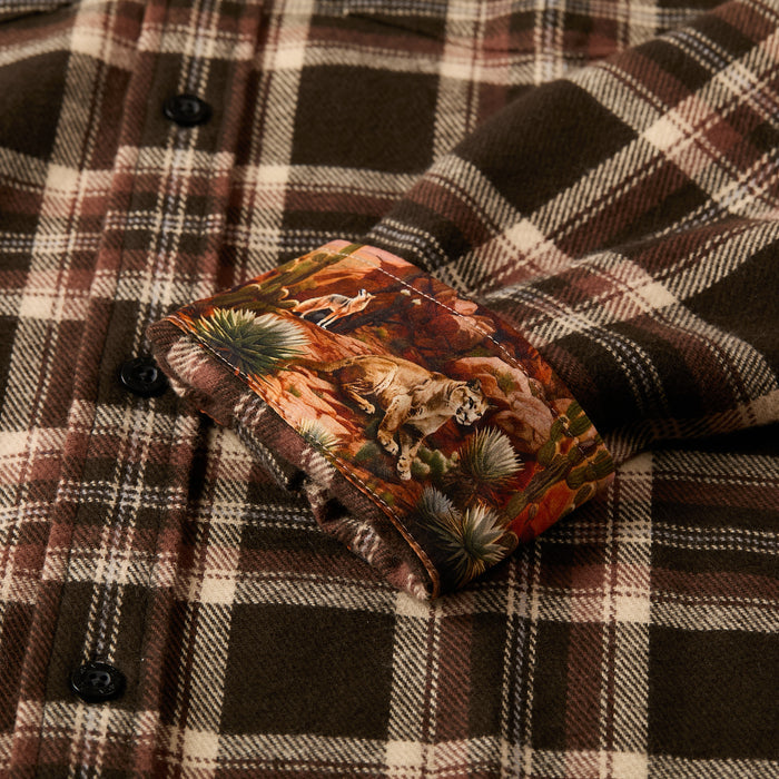 A close-up of the Men's Workhorse Elite Flannel Shirt in Diamondback Brown shows its black buttons and a turned-up cuff revealing a colorful inner lining with animals and desert plants.