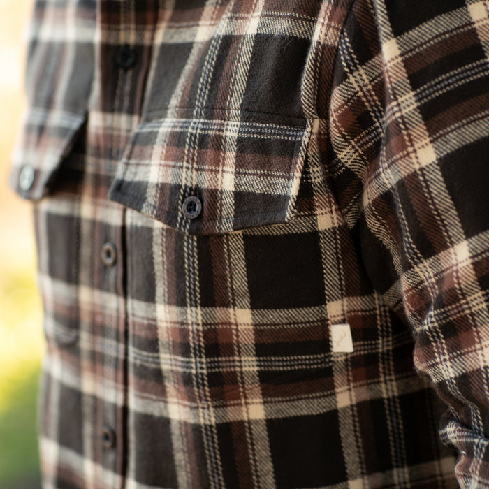 A close-up of a person wearing the Men's Workhorse Elite Flannel Shirt- Diamondback Brown, featuring buttoned chest pockets and visible heavyweight cotton fabric with brown and black plaid details.