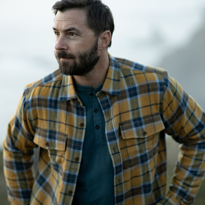 Bearded man in Pladra Men's Workhorse Elite Flannel Shirt—Easton Gold stands outside, gazing thoughtfully to the side.