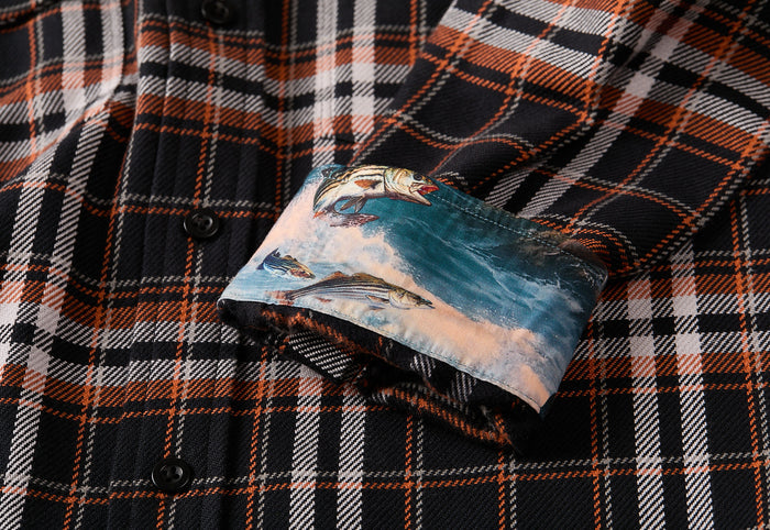A close-up of the Men's Workhorse Elite Flannel Shirt- Posey Black showing its black, orange, and white plaid design with a cuff folded to reveal a vibrant inner lining featuring fish swimming in water.