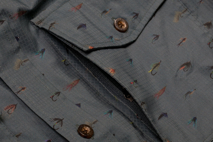 Close-up of the Men's Yuba Fishing Shirt - Flies Print, featuring brown buttons, a pocket, and a colorful fishing flies pattern. Made from quick-drying fabric for comfort on the water.