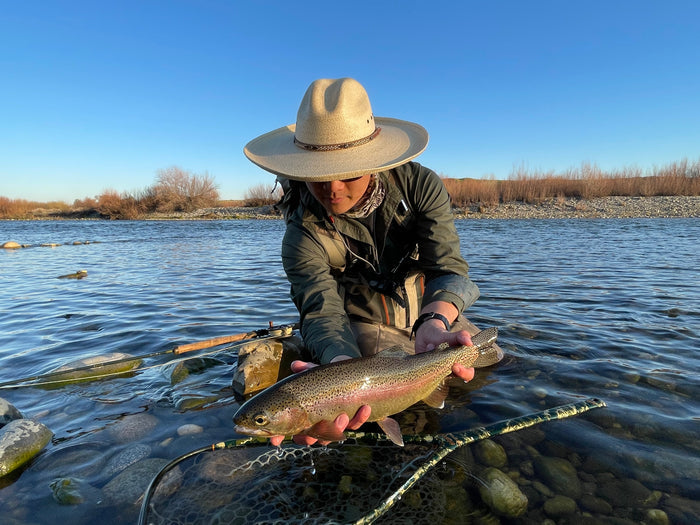 Man in hat holds a trout over shallow river, wearing Pladra Men's Yuba Fishing Shirt - Kombu Green, UPF 50+.