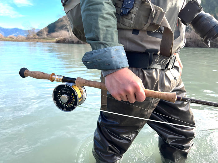 Wearing Pladra Men's Yuba Fishing Shirt - Kombu Green, person in waders holds fly rod, camera on chest.