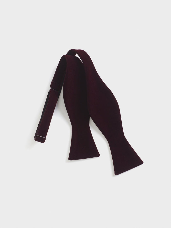 Merlot velvet self-tie bow tie, untied and laid flat on a grey background.