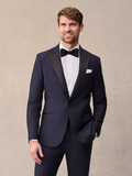 A man in a midnight blue tuxedo with black satin peak lapels, black bow tie, and white pocket square.