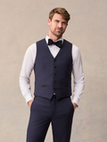 Man in midnight blue tuxedo vest over white shirt with black bow tie, hands in pockets, full length
