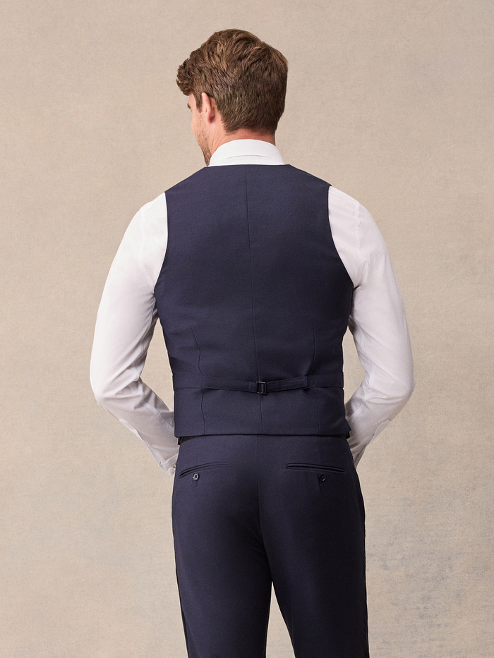 Back view of man in midnight blue tuxedo vest with satin strap and buckle over white shirt