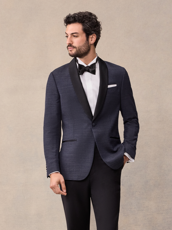 Man in midnight pin-dot tuxedo jacket with black satin shawl lapel and black bow tie, tan backdrop