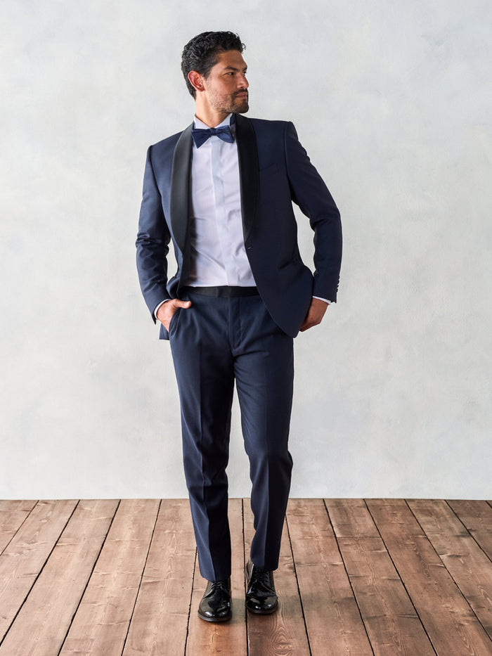 Man in midnight shawl-lapel tuxedo, black satin lapel and bow tie, hands in pockets, three-quarter view