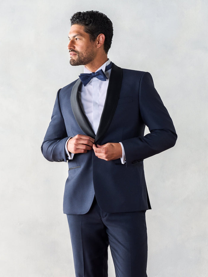 Close-up of man in midnight shawl-lapel tuxedo, black satin lapel, buttoning jacket, looking away