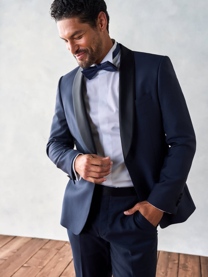 Man in midnight shawl-lapel tuxedo jacket, black satin lapel and bow tie, smiling, hand in pocket